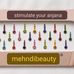 Può includere: Una confezione rettangolare contenente ventiquattro piccoli adesivi bindi multicolori disposti in file. La scatola riporta il testo "stimulate your anjana" e "mehndibeauty" accanto all'immagine di una persona.