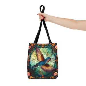 May include: A black tote bag with a colorful stained glass design featuring a hummingbird in flight. The design is surrounded by a floral border.
