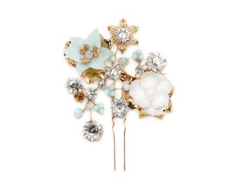 May include: A gold hair comb with white and light blue flowers, rhinestones, and beads. The comb has two gold pins.