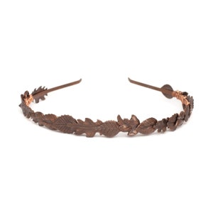 Puede incluir: Una diadema de cobre con un diseño de hojas. La diadema está hecha de metal fino y tiene un aspecto delicado y femenino.