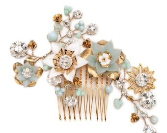 May include: A gold hair comb with a floral design. The comb is decorated with white and light blue flowers, rhinestones, and gold beads.