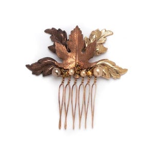 Op de afbeelding: Een gouden en bruine bladeren haar kam met parel en gouden accenten. De kam heeft een decoratief ontwerp van bladeren en is perfect om elke haarstijl een vleugje elegantie te geven.