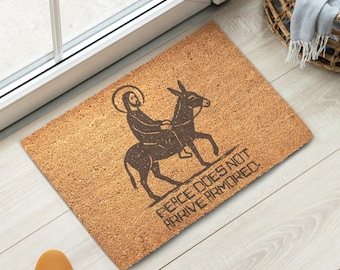 Felpudo de Jesús con ilustración original, texto "La paz no llega blindada", material resistente.