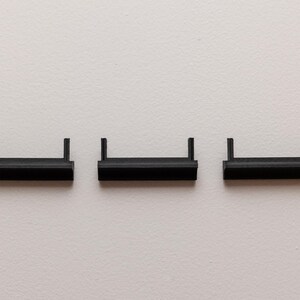 Puede incluir: Tres peque&ntilde;as estanter&iacute;as rectangulares negras con bordes elevados est&aacute;n dispuestas horizontalmente sobre un fondo blanco. Cada estanter&iacute;a tiene dos soportes verticales. Las estanter&iacute;as parecen ser de pl&aacute;stico o un material similar.