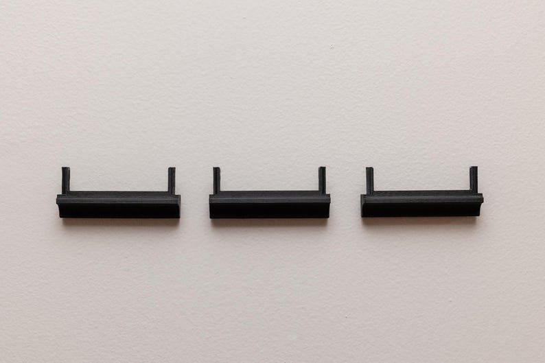 Puede incluir: Tres peque&ntilde;as estanter&iacute;as rectangulares negras con bordes elevados est&aacute;n dispuestas horizontalmente sobre un fondo blanco. Cada estanter&iacute;a tiene dos soportes verticales. Las estanter&iacute;as parecen ser de pl&aacute;stico o un material similar.