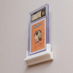 Puede incluir: Una tarjeta coleccionable calificada en una funda de pl&aacute;stico transparente, montada en un expositor de pared blanco. La tarjeta presenta una ilustraci&oacute;n de p&aacute;jaro de dibujos animados y texto japon&eacute;s. La funda est&aacute; calificada con un 10.