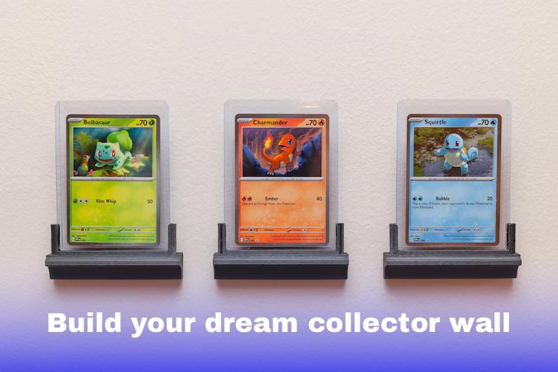 Puede incluir: Tres cartas Pok&eacute;mon enmarcadas con Bulbasaur, Charmander y Squirtle, expuestas en estantes negros individuales. Las cartas est&aacute;n en fundas protectoras. El texto en la parte inferior dice "Build your dream collector wall."
