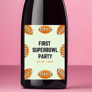May include: A black wine bottle with a label that says "First Superbowl Party as Mr. & Mrs." The label is decorated with orange footballs.