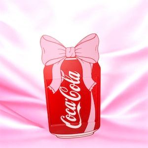 May include: A red Coca-Cola can-shaped design with a pink bow at the top. The Coca-Cola logo is in white script. The background is a pink, silky fabric.