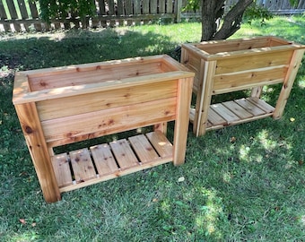 May include: Two wooden raised garden beds with a shelf underneath. The beds are made of natural cedar wood and are stained a light brown color.