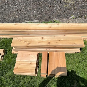 May include: A pile of unfinished cedar wood planks, ready for a woodworking project. The planks are stacked in a variety of sizes and lengths, with some of the planks being cut into smaller pieces.