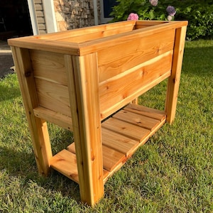 以下が含まれることがあります： 棚の下に棚が付いた木製の高床式菜園。ベッドは天然のヒノキ材で作られており、素朴な外観をしています。