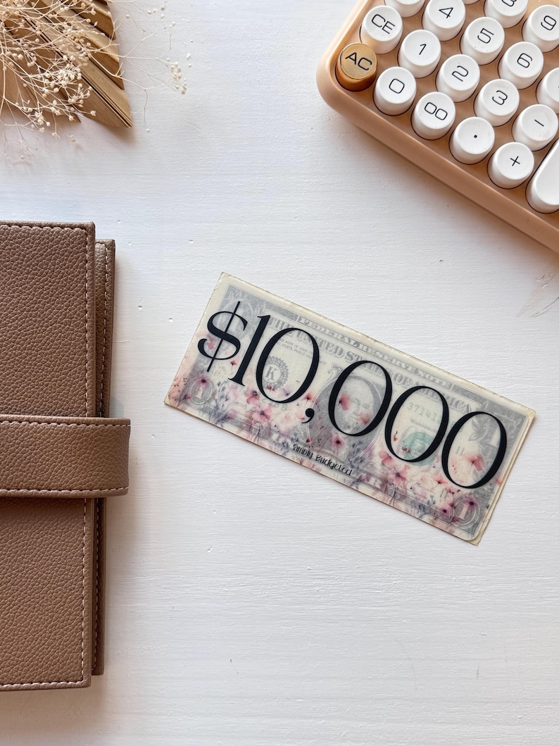 May include: A close-up of a $10,000 bill with a floral design. The bill is printed on a white background with pink flowers.