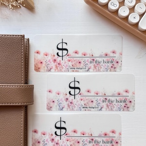 May include: Three floral patterned stickers with a dollar sign and the text "in the bank" and "Simply Budgeted".