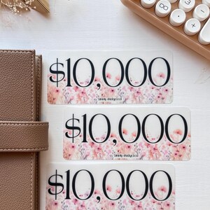 May include: Three transparent stickers with a floral design and the text "$10,000" and "Simply Budgeted" printed on them.