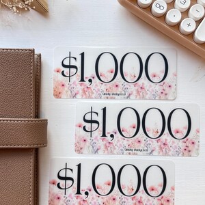 May include: Three pink and white floral patterned stickers with the text "$1,000" in black. The text "Smoky Bucketed" is printed in smaller font below the dollar amount on each sticker.