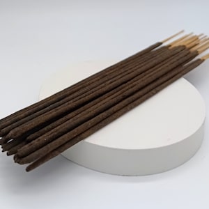 Op de afbeelding: Een bundel bruine wierookstokjes met een lichtbruine houten kern. De stokjes zijn netjes op een ronde witte ondergrond gestapeld.