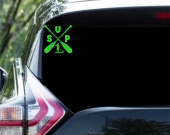 Könnte beinhalten: Grüner Vinyl-Aufkleber mit dem Wort "SUP" und einer Silhouette einer Person beim Paddelsurfen. Der Aufkleber befindet sich auf der Heckscheibe eines schwarzen Autos.