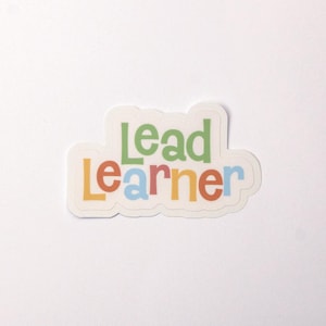 May include: A white sticker with the words "Lead Learner" in colorful letters. The letters are in different colors, including yellow, orange, red, blue, and green.