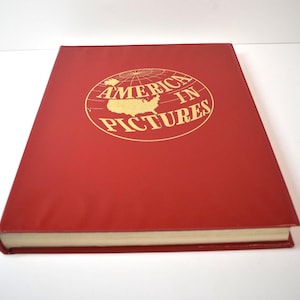 May include: A red hardcover book titled "America in Pictures." The title is in gold lettering, with a gold outline of the United States within a globe. The book has a clean, minimalist design.