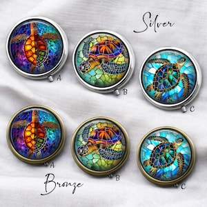 May include: Round silver and bronze pill cases with colorful stained-glass turtle designs. Each case features a different turtle design, with variations in color and pattern. The word "Silver" and "Bronze" are written above and below the cases.