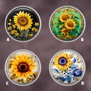 May include: Four round, silver-rimmed cabochons with sunflower designs. One features a yellow sunflower on a black background, another has sunflowers on a teal background with gold filigree, a third shows a sunflower on a wood-grain background, and the last has a sunflower with blue accents.