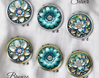 May include: A collection of six round compact mirrors with floral designs. The mirrors are in silver and bronze tones, with intricate patterns in shades of blue, white, and gold. The word "Silver" and "Bronze" are written above the mirrors.