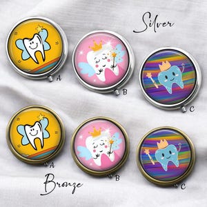 May include: A collection of round pill cases with cartoon tooth designs. The cases are available in silver and bronze finishes. Each case features a different tooth character with wings, a crown, or a magic wand, set against colorful backgrounds.