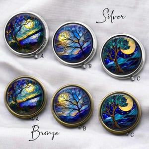 Op de afbeelding: Een verzameling ronde pillendoosjes met een ontwerp met een natuurthema. De doosjes zijn verkrijgbaar in zilver en brons, elk met een kleurrijke illustratie van een boom, maan en landschap. De woorden "Silver" en "Bronze" staan op de afbeelding.
