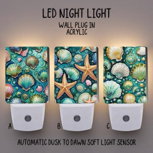 May include: Three LED night lights with seashell designs. Each has a white base and a rectangular acrylic cover with a different seashell pattern in shades of blue, green, pink, and gold. Text on the image reads "LED NIGHT LIGHT, WALL PLUG IN ACRYLIC, AUTOMATIC DUSK TO DAWN SOFT LIGHT SENSOR."