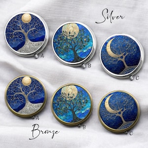 May include: Round compact mirrors with tree of life designs. The mirrors are available in silver and bronze finishes. Each mirror features a detailed tree design with a moon or crescent moon against a blue background. The word "Silver" and "Bronze" are written on the image.