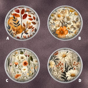 May include: Four round, silver-rimmed decorative cabochons with floral and botanical designs. The designs include autumn leaves, flowers, and plants in shades of orange, yellow, and white. The cabochons are set against a brown background.