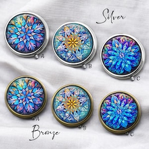 May include: A collection of six round pill cases with floral designs. Three cases have silver rims, and three have bronze rims. The floral patterns feature shades of blue, purple, and yellow. The word "Silver" and "Bronze" are written above the cases.