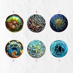 May include: A collection of six iridescent glass buttons in various colors and designs. The buttons are round with intricate patterns, including floral and geometric motifs. Colors range from green and gold to blue and purple.