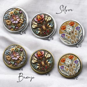 Pode incluir: Espelhos compactos prateados e bronze com desenhos florais. Os espelhos prateados apresentam padrões florais detalhados em várias cores, enquanto os espelhos de bronze têm desenhos semelhantes. As palavras "Silver" e "Bronze" estão escritas acima e abaixo dos espelhos.