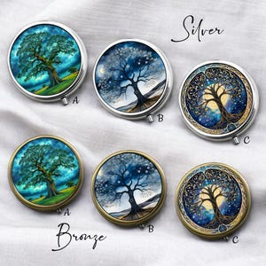 Könnte beinhalten: Runde silberne und bronzefarbene Pillendosen mit Lebensbaum-Designs. Die Dosen zeigen verschiedene Baumillustrationen vor farbenfrohen Hintergründen, darunter eine lebendige grüne Landschaft, eine Sternennacht und eine Winterszene. Die Wörter "Silver" und "Bronze" sind auf dem Bild geschrieben.
