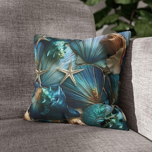 Op de afbeelding: Een vierkant sierkussen met een levendige print van diverse schelpen en zeesterren in tinten diepblauw, turquoise en goud. Het ontwerp toont een gedetailleerde compositie van waaiervormige schelpen, spiraalvormige zeeslakken en zeesterren.