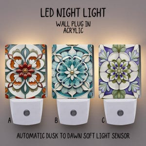 Könnte beinhalten: Drei LED-Nachtlichter aus Acryl mit floralen Designs in Orange, Türkis und Lila. Jedes Nachtlicht hat einen weißen Sockel und den Text "LED NIGHT LIGHT" und "AUTOMATIC DUSK TO DAWN SOFT LIGHT SENSOR".