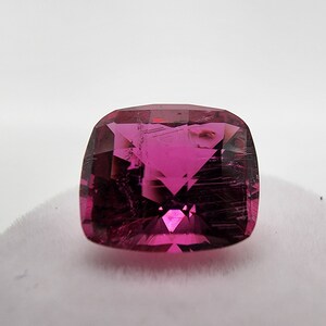 K&ouml;nnte beinhalten: Ein leuchtend rosa Edelstein mit einem Kissen-Schliff. Der Edelstein hat eine klare, facettierte Oberfl&auml;che und ist vor einem wei&szlig;en Hintergrund platziert.