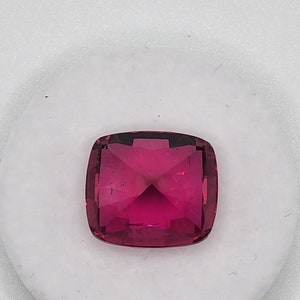 K&ouml;nnte beinhalten: Ein leuchtend rosa Edelstein mit einem Kissen-Schliff. Der Edelstein ist facettiert und hat einen hohen Glanz.