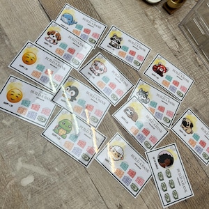 Puede incluir: Un conjunto de tarjetas blancas con ilustraciones coloridas de animales y emojis. Cada tarjeta tiene el texto "BUILD A BANK" y "HAPPY 1.00". Las tarjetas presentan una variedad de diseños, incluyendo un perro, una ballena, un mapache y un cerdo.