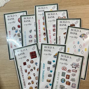 May include: A collection of rectangular cards with various themes, each featuring the text "BUILD A BANK" and "savings challenge." The cards have different illustrations and titles like "Choco Cravings" and "Annual Leave."