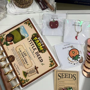 May include: A spiral-bound notebook with a Build a Farm Title Deed cover, a red pepper enamel pin, a gold-tone chili pepper charm, a pack of fruit stickers, a seed packet card, two dice, a ring, and two lip treatment tubes on a white surface.