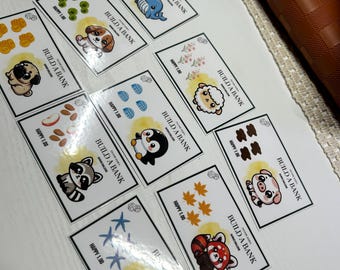 May include: A collection of rectangular cards with cartoon animal illustrations, including a whale, puppy, sheep, penguin, raccoon, pig, turtle, and red panda. Each card has the text "BUILD A BANK" and "HAPPY 1.00".