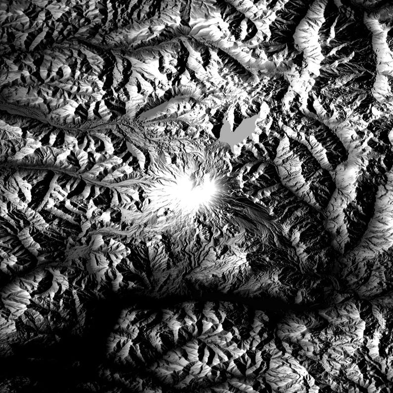 May include: A grayscale topographical map of a mountainous region. The image features a prominent, bright peak surrounded by textured terrain, valleys, and a lake. The lighting creates shadows and highlights, emphasizing the elevation changes.