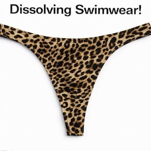 Puede incluir: Braguita de bikini tipo tanga con estampado de leopardo. El traje de baño es de color beige con manchas marrones oscuras. El texto "Dissolving Swimwear!" está en la parte superior de la imagen.