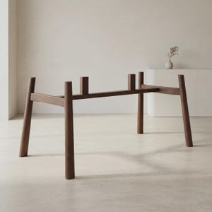 May include: A dark brown wooden table base featuring four tapered legs connected by a horizontal support beam. The structure includes two vertical rectangular mounting blocks positioned along the center rail to support a tabletop surface.