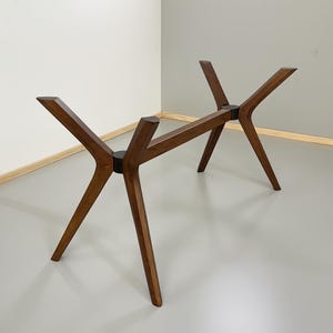 May include: A wooden table base in a mid-century modern style. The dark brown wood base has a starburst design with angled legs. The base is approximately 76 cm long and 51 cm wide, suitable for a dining or coffee table.