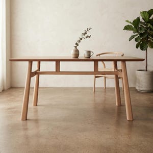 May include: A light-toned wooden dining table with four tapered legs and a horizontal support frame. On the table sits a small ceramic vase containing a single leafy branch and a matching ceramic mug. A wooden chair is tucked behind the table.