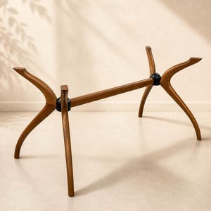 May include: A wooden table base with a mid-century modern design. The base features four curved legs and a central support beam, all in a warm brown tone. Black connectors join the legs and beam.